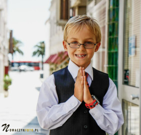 Sesja komunijna chłopca stojącego z uliczce z rękami złożonymi do modlitwy